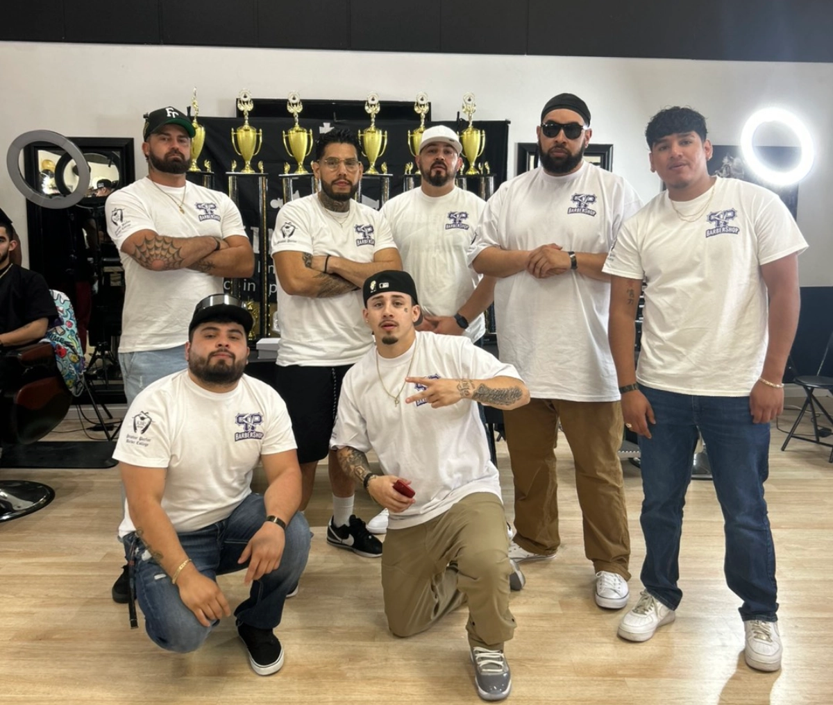 A group of men posing together in matching white shirts indoors.